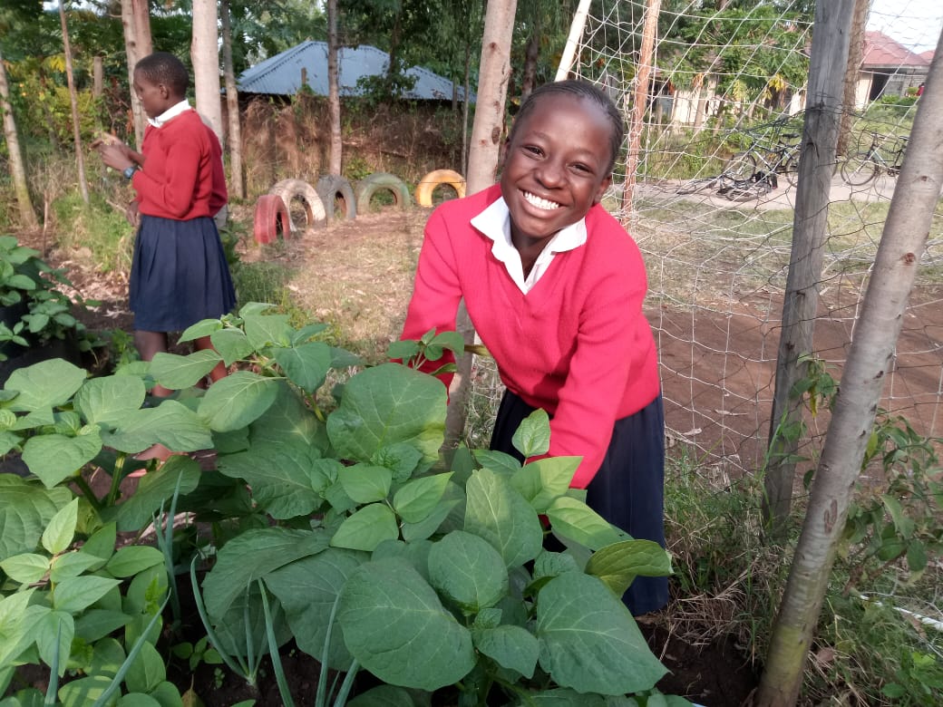 A smiling primary school pupil beside a thriving conical garden