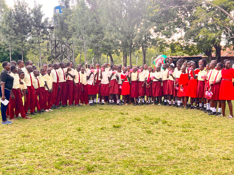 Schoolchildren standing in a line, some holding packets of sanitary pads
